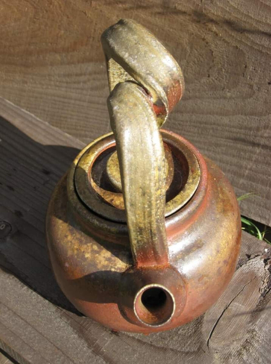 Woodfired teapot (2016) Woodfired teapot by Shane Brodie with a mottled red and tan surface created from the wood ash. The oversized handle has a large looping twist in it.