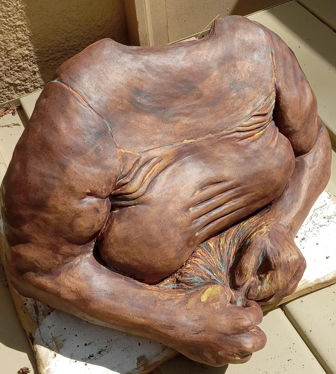 Maker Sculpture of the torso and arms of a queer woman by Shane Brodie. Her hands are in front and pulling something coming from her torso. Wrinkles, folds and other surface features are emphasized by the application of multiple stains.