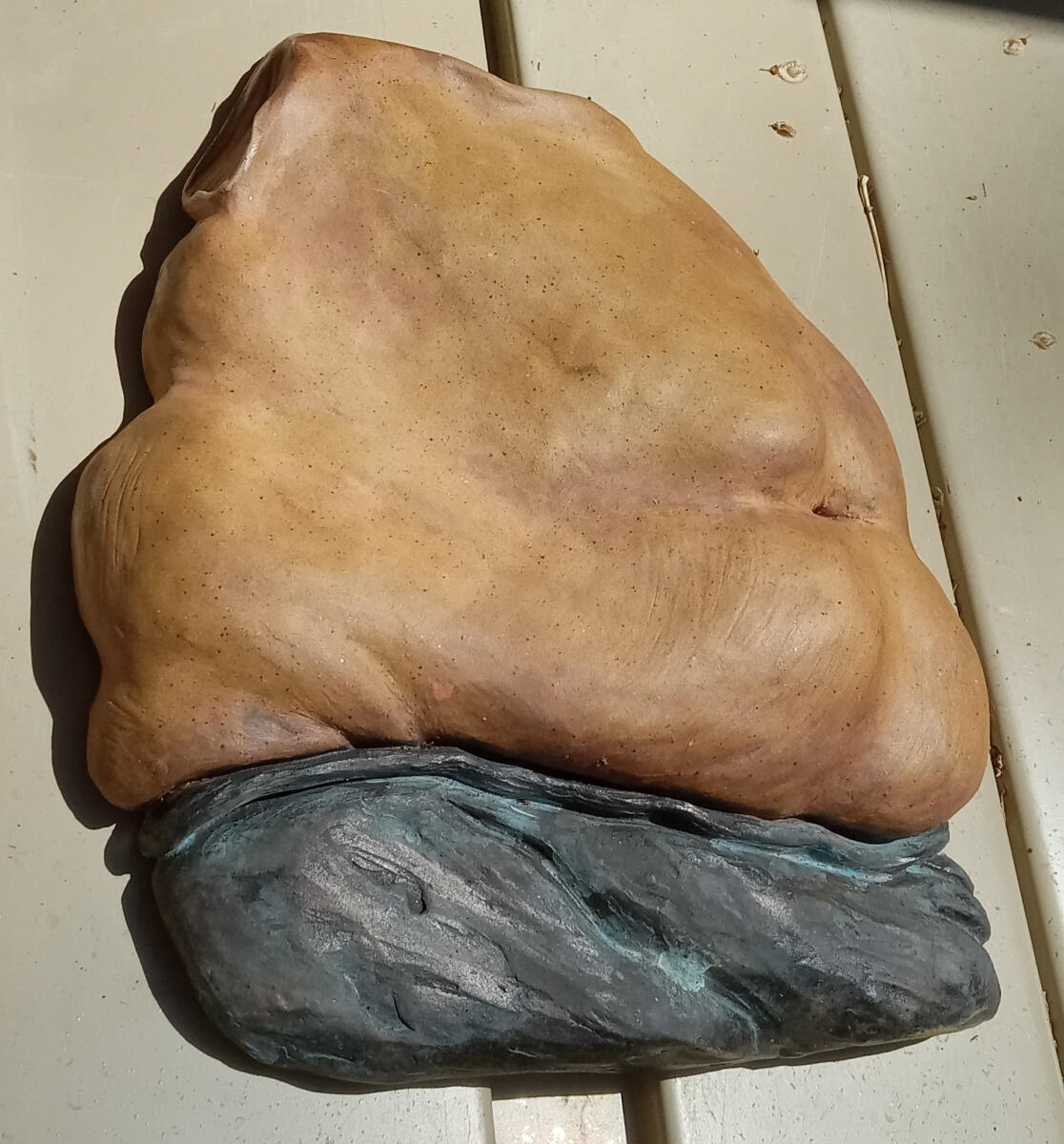 Nonbinary 3 Bas relief sculpture by Shane Brodie depicting a round belly and right hip with stretch marks. Overall, the piece is a speckled golden-brown color meant to depict naked skin. Below the belly, the person is wearing black pants with folds highlighted in ligh