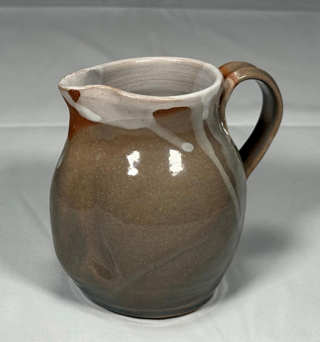 Creamer A creamer (a small, short, round pitcher) with a light green glazed body and a white liner. There are also some spots of white glaze and unglazed red clay near the rim of the piece.